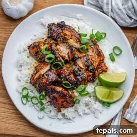 slow cooker chicken thighs served over rice on a plate and then topped with sliced green onions.